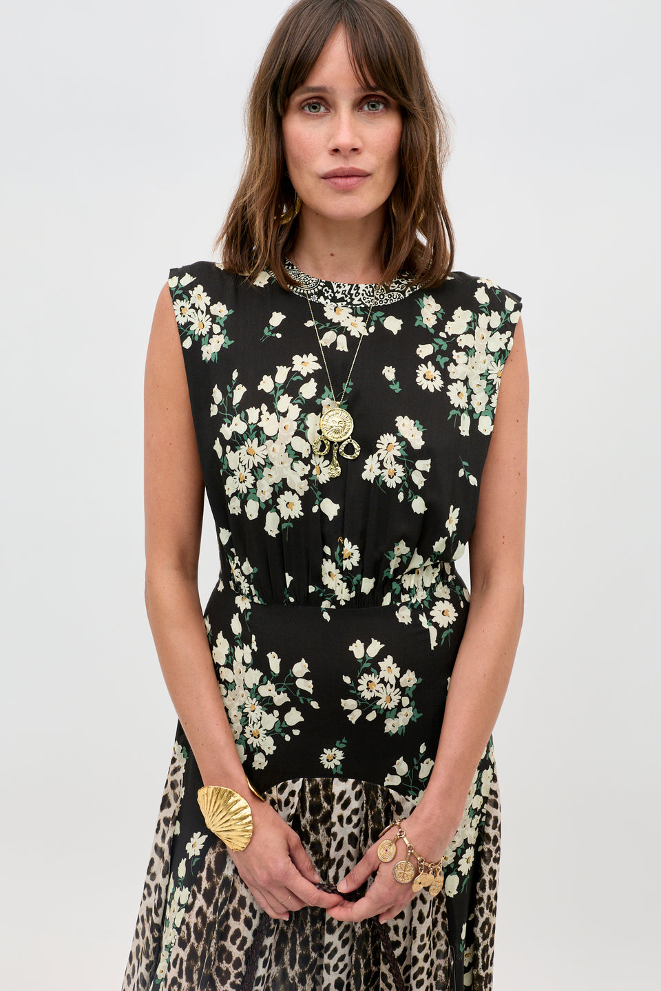 Woman wearing the Coralie - Amelia Gremlin Mix Black sleeveless dress featuring a white floral print top and leopard print skirt, styled with layered necklaces and gold jewelry, standing against a plain light gray background.