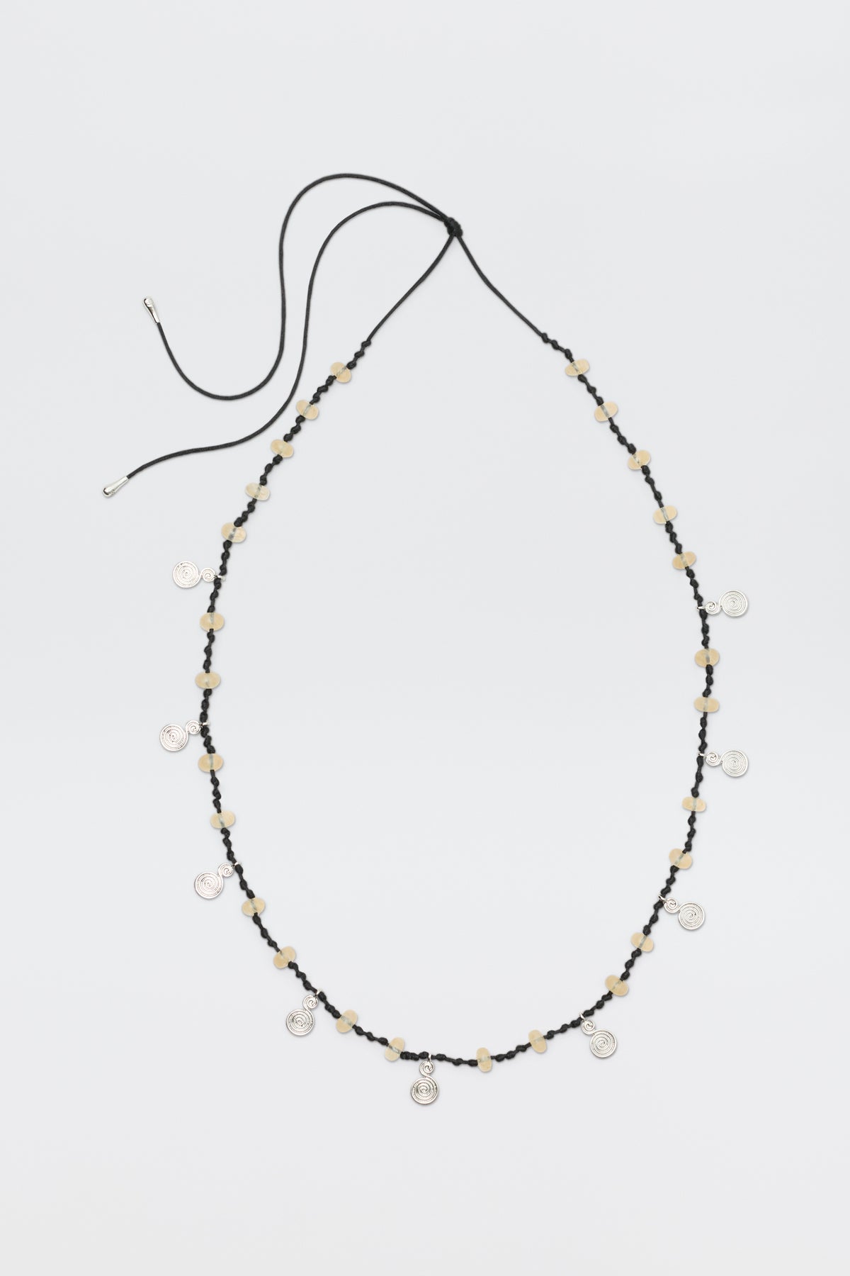 A long black cord necklace called "Mikah - Silver," featuring beige beads and small round silver charms evenly spaced, is displayed on a plain white background with the cord ends untied.