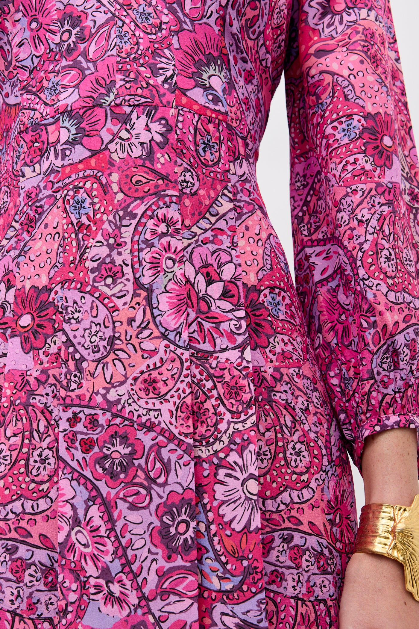 A close-up of a person wearing the Camellia - Paisley Floral Red long-sleeved dress, featuring vibrant pink, purple, and red florals and paisleys, paired with a chunky gold bracelet.