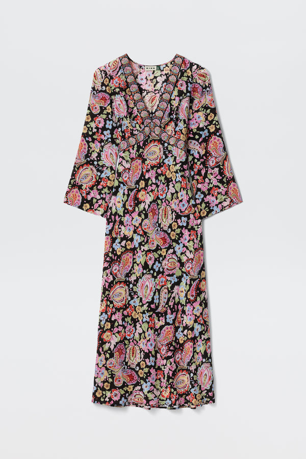 The Tania - Cara Floral Black is a long-sleeved V-neck maxi dress with a vibrant floral and paisley pattern on a black background, shown flat on a white surface.