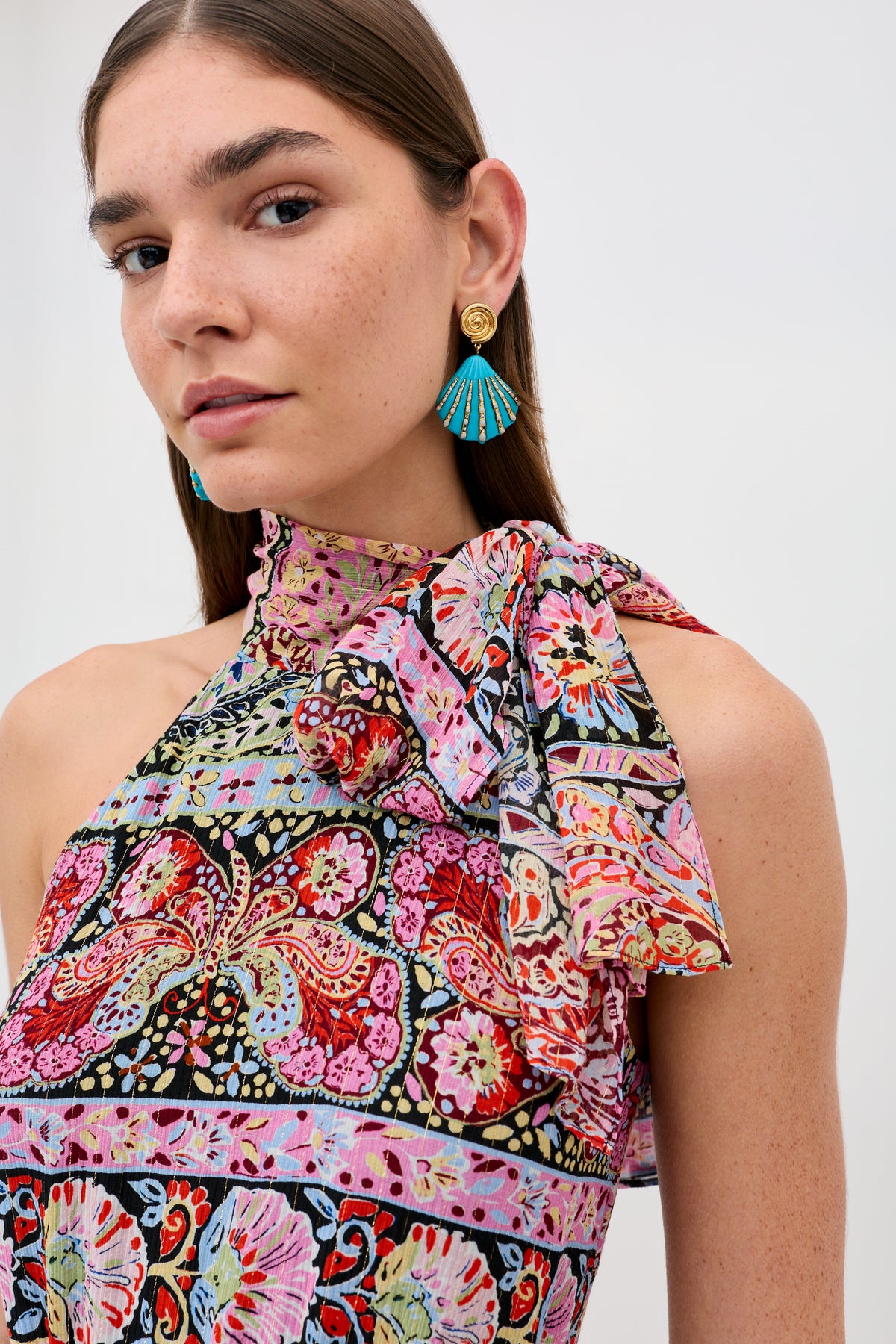 A woman with straight brown hair confidently poses in the Abi - Cara Stripe Black dress, featuring bold stripes and a large bow on one shoulder. She pairs it with blue fan-shaped earrings and stands against a plain background.