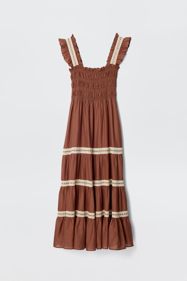The Aubrie - Brown dress features ruffled straps, a smocked bodice, and a tiered skirt with cream lace crochet midi details, shown against a plain white background.