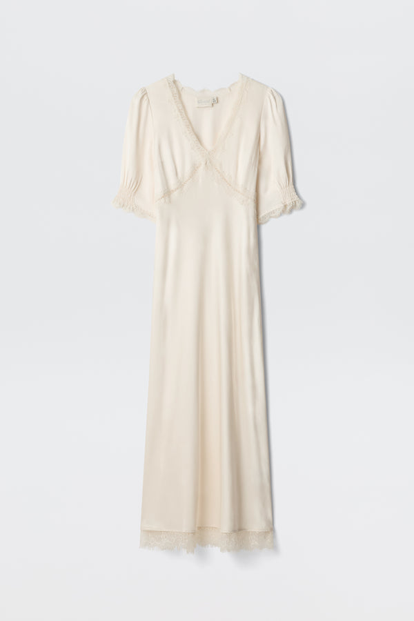 The Annina - Pearl is a cream satin dress with short puff sleeves, lace-trimmed neckline, sleeves, and hem, plus a subtle v-neckline. This vintage-inspired piece exudes elegant charm.