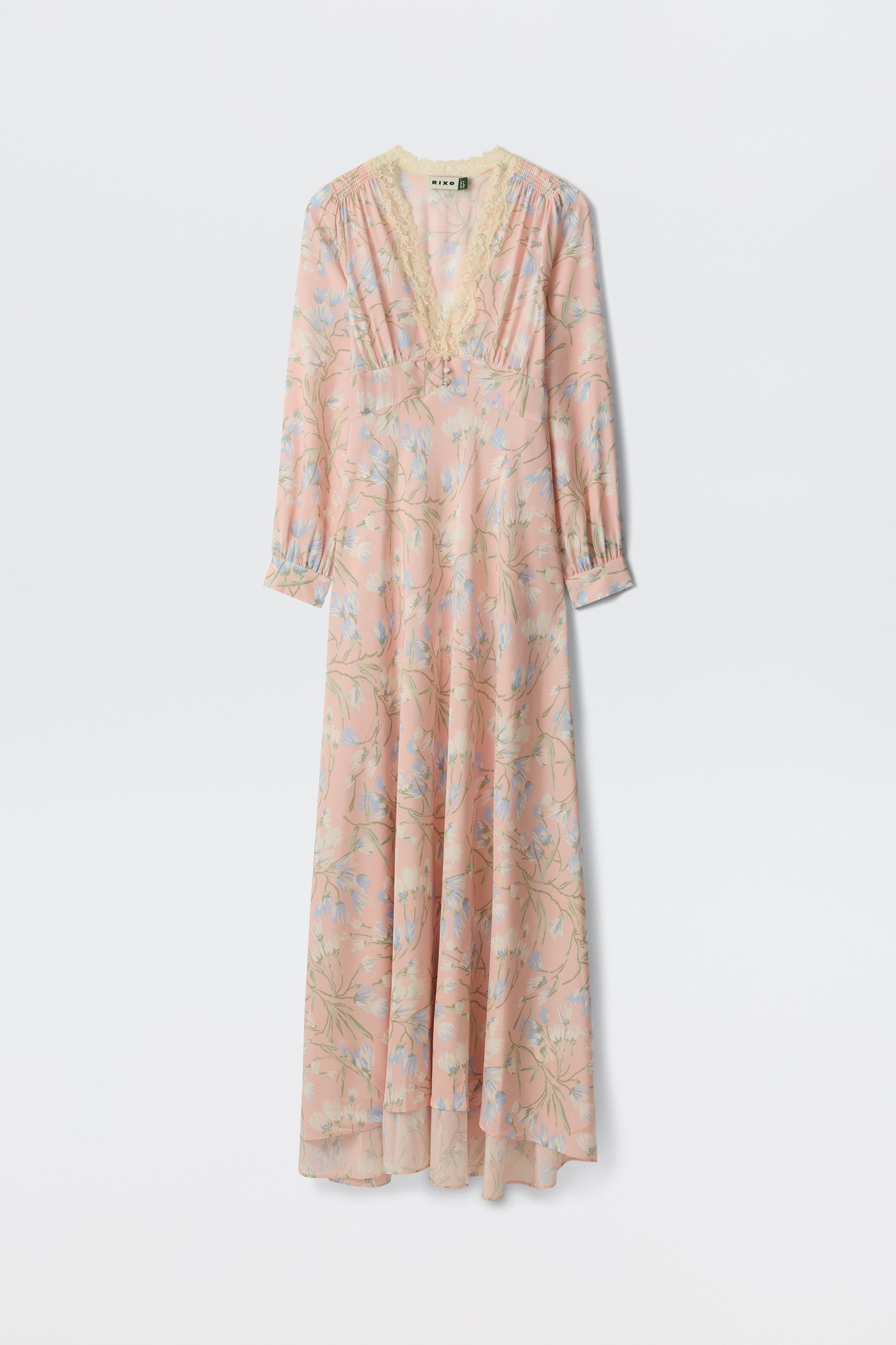 The Emory - Watercolour Floral Pink is a long, light pink dress featuring blue and green floral patterns, long sleeves, a lace-trimmed V-neckline, and an airy, flowing silhouette.
