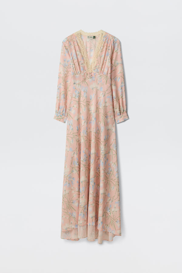 The Emory - Watercolour Floral Pink is a long, light pink dress featuring blue and green floral patterns, long sleeves, a lace-trimmed V-neckline, and an airy, flowing silhouette.
