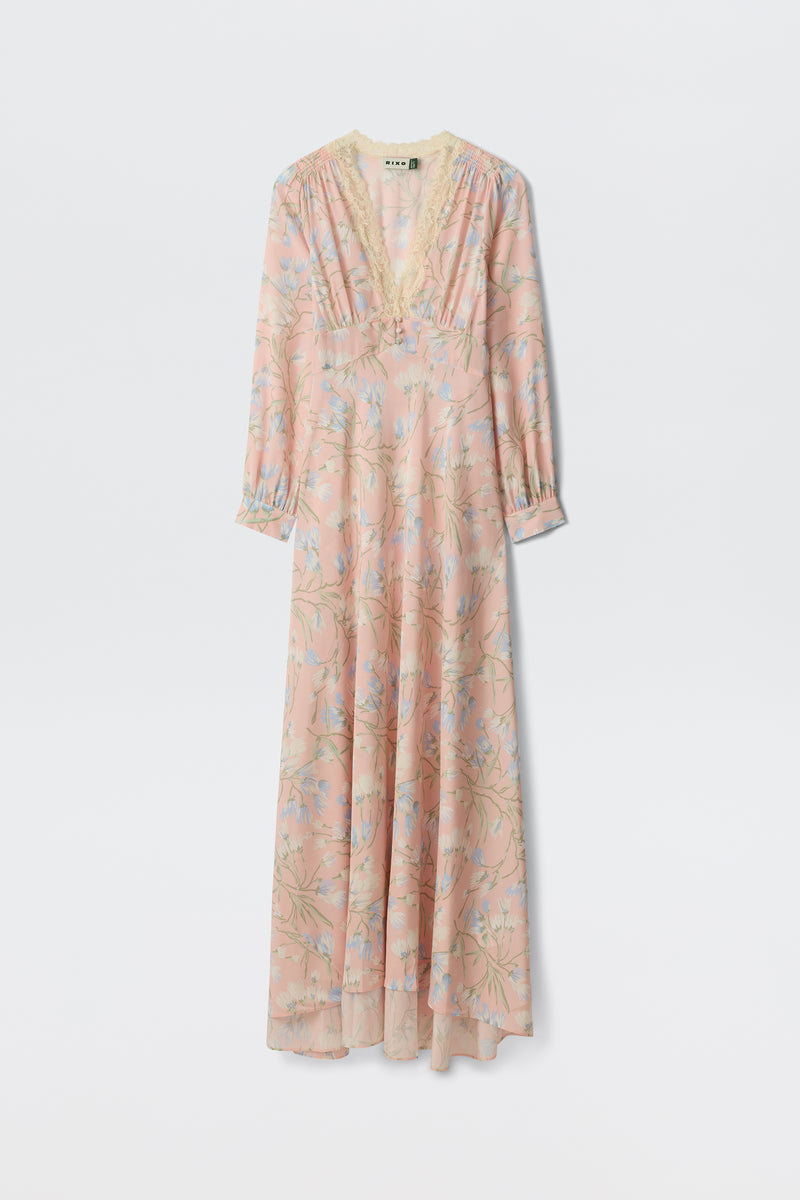 The Emory - Watercolour Floral Pink is a long, light pink dress featuring blue and green floral patterns, long sleeves, a lace-trimmed V-neckline, and an airy, flowing silhouette.