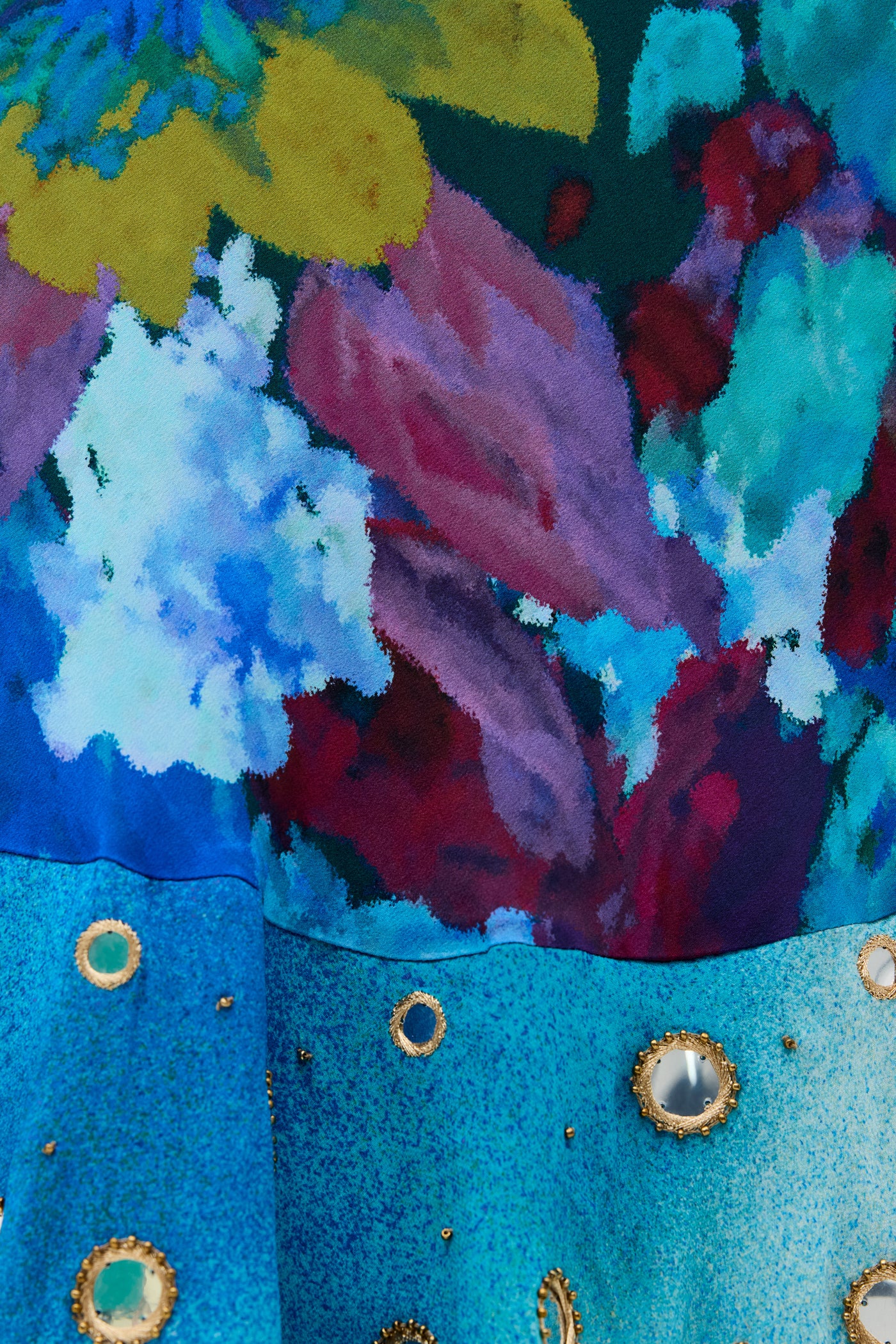 Introducing Ordinia - Jessica Bouquet Mix Blue: This colorful floral fabric features vibrant blue, yellow, red, and green patterns reminiscent of a Liberty London print. The lower section showcases turquoise material adorned with round gold and silver studs or mirrored accents. Bold and artistic, the design is rich in texture and color—an inspired choice for statement style at black-tie weddings.