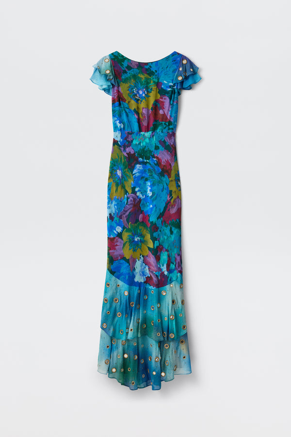 A long, short-sleeved Ordinia - Jessica Bouquet Mix Blue gown with a vibrant Liberty London floral print in blue, green, and purple hues features a sheer ruffled hem adorned with small circular accents—perfect for black-tie weddings—shown against a plain light background.