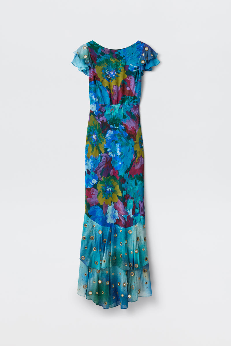 A long, short-sleeved Ordinia - Jessica Bouquet Mix Blue gown with a vibrant Liberty London floral print in blue, green, and purple hues features a sheer ruffled hem adorned with small circular accents—perfect for black-tie weddings—shown against a plain light background.