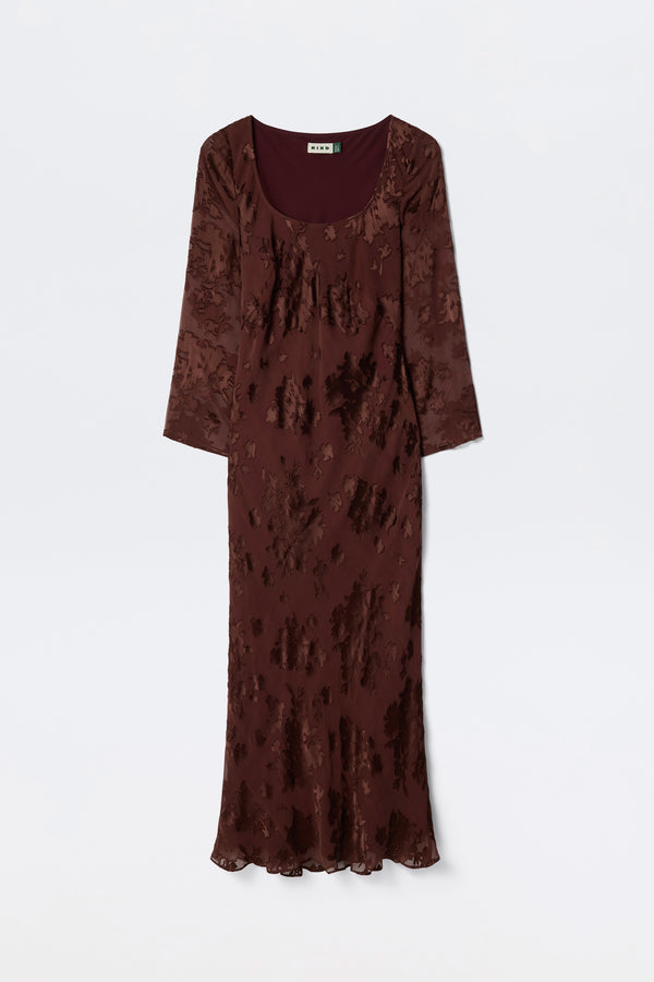 The Noraya - Bouquet Devoré Brown is a long, fitted maroon dress with long sleeves, a scoop neckline, and a subtle textured floral pattern, shown against a plain white background.