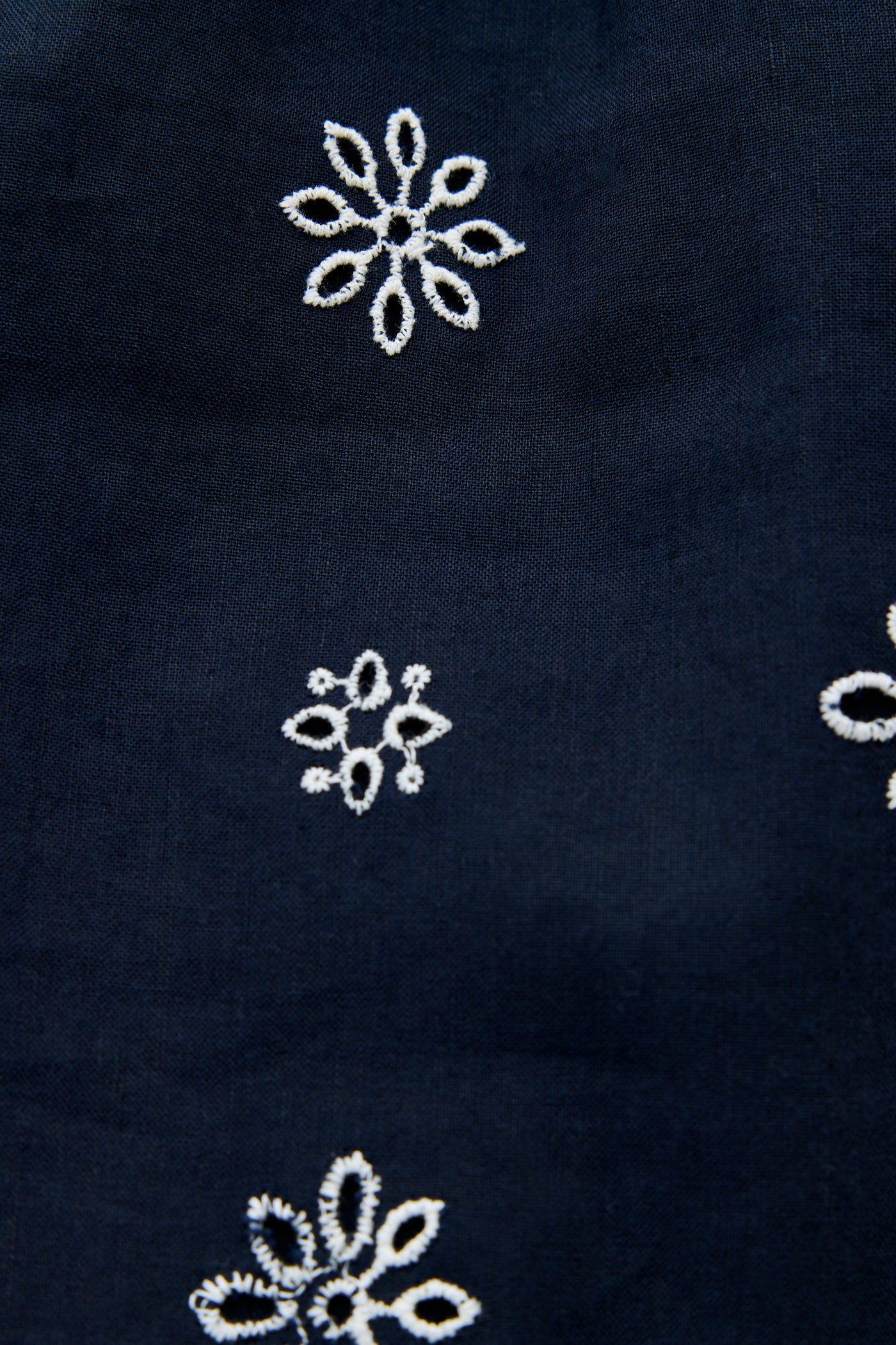 Susana - Blossom Cutwork Embroidery Navy: A navy linen-cotton mini dress adorned with white blossom cutwork embroidery arranged organically across the fabric, featuring delicate white lace details inspired by classic broderie anglaise styles.