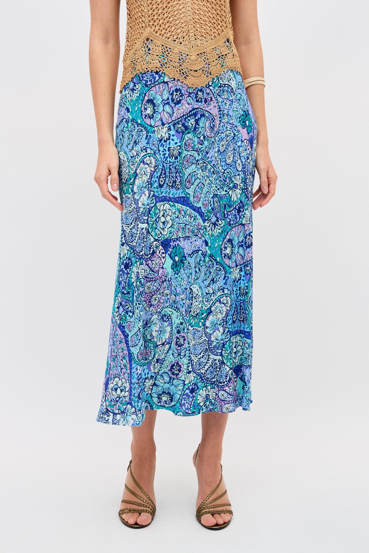 A person stands facing forward, wearing the Kelly - Paisley Floral Blue midi skirt. Only their lower half is visible, paired with strappy sandals and a bracelet.