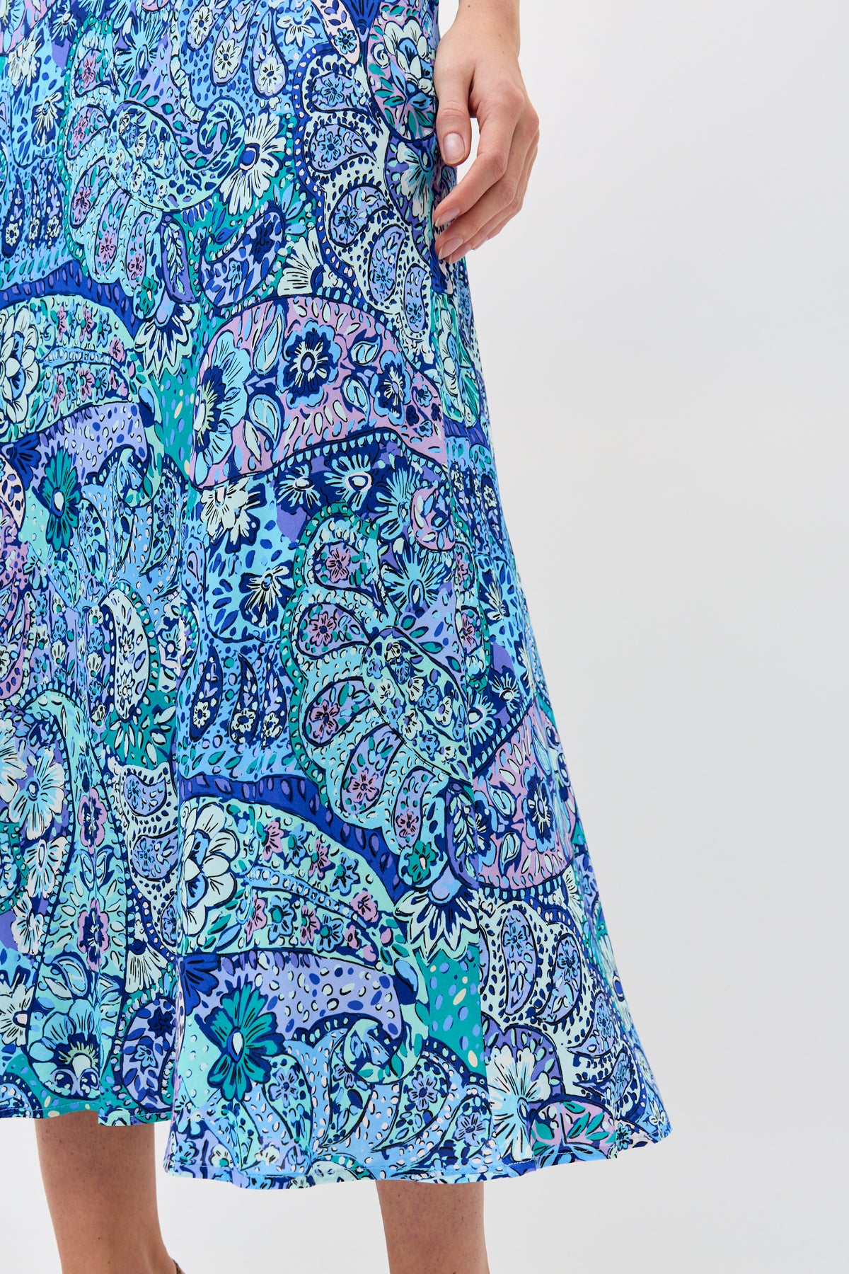 A person wearing the Kelly - Paisley Floral Blue skirt stands against a plain light background, with only their hand and lower body visible.