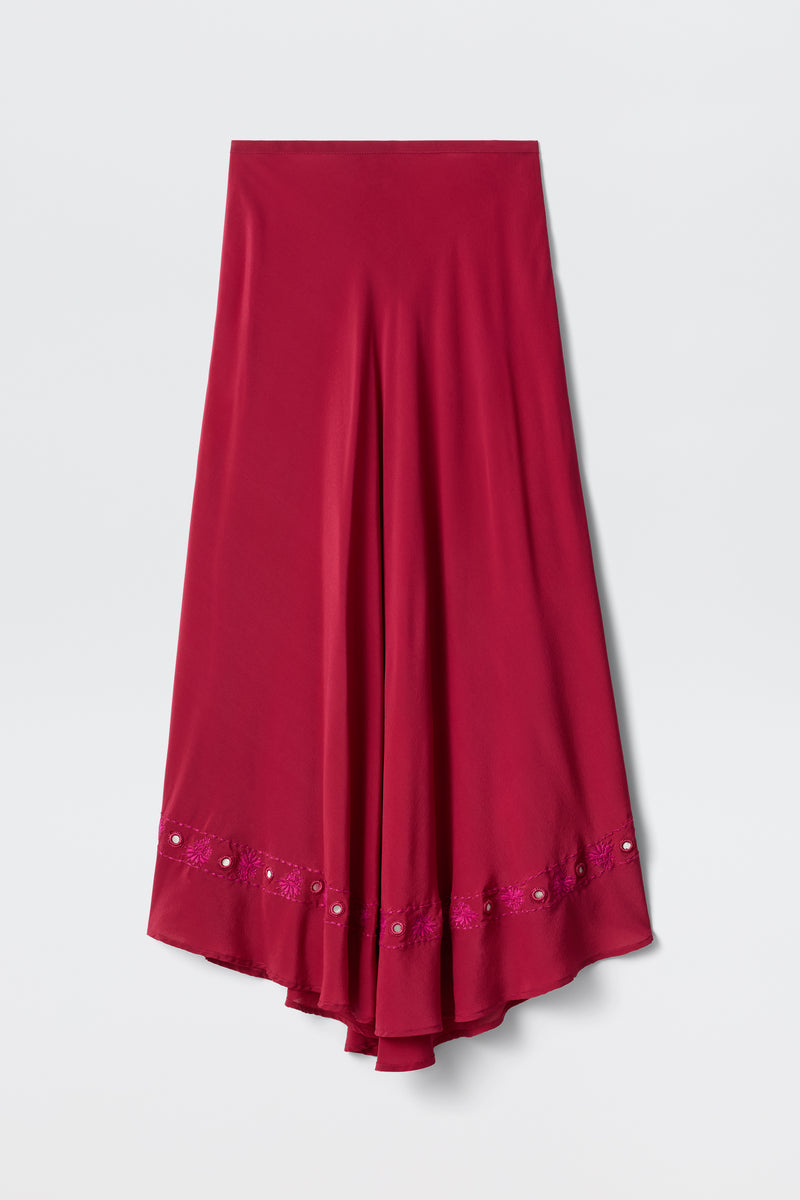 The Rudy - Mirror Embellishment Magenta Pink is a long, deep magenta pink satin skirt with an asymmetrical hem. Decorative embroidery and mirror embellishments accent the lower edge of the skirt, which is displayed against a plain white background.