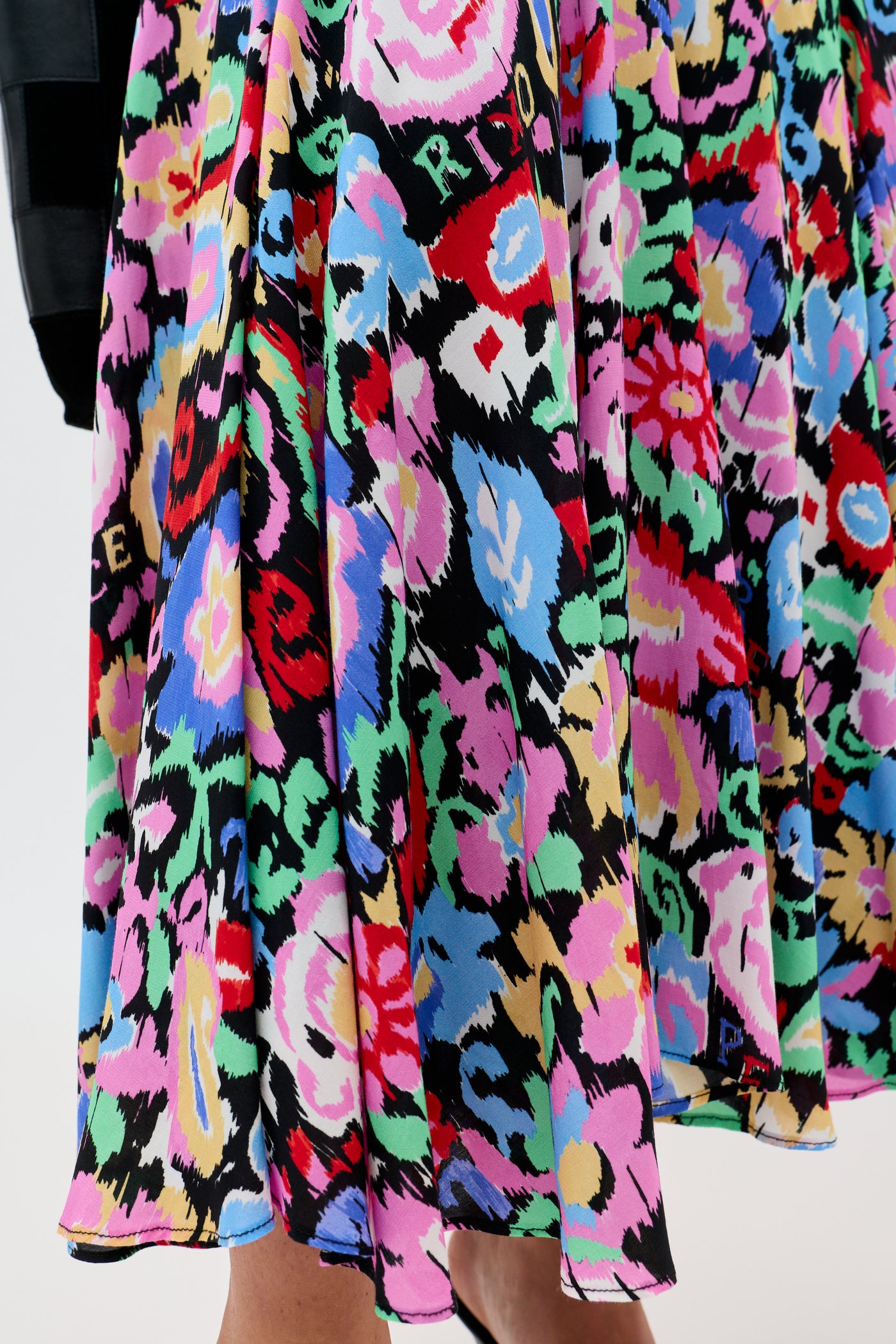 A close-up of the Libbie - Ikat Bloom Charcoal skirt, showcasing bold abstract floral and geometric patterns in vibrant red, pink, purple, blue, green, yellow, and black on soft-flowing fabric around the wearer’s legs.