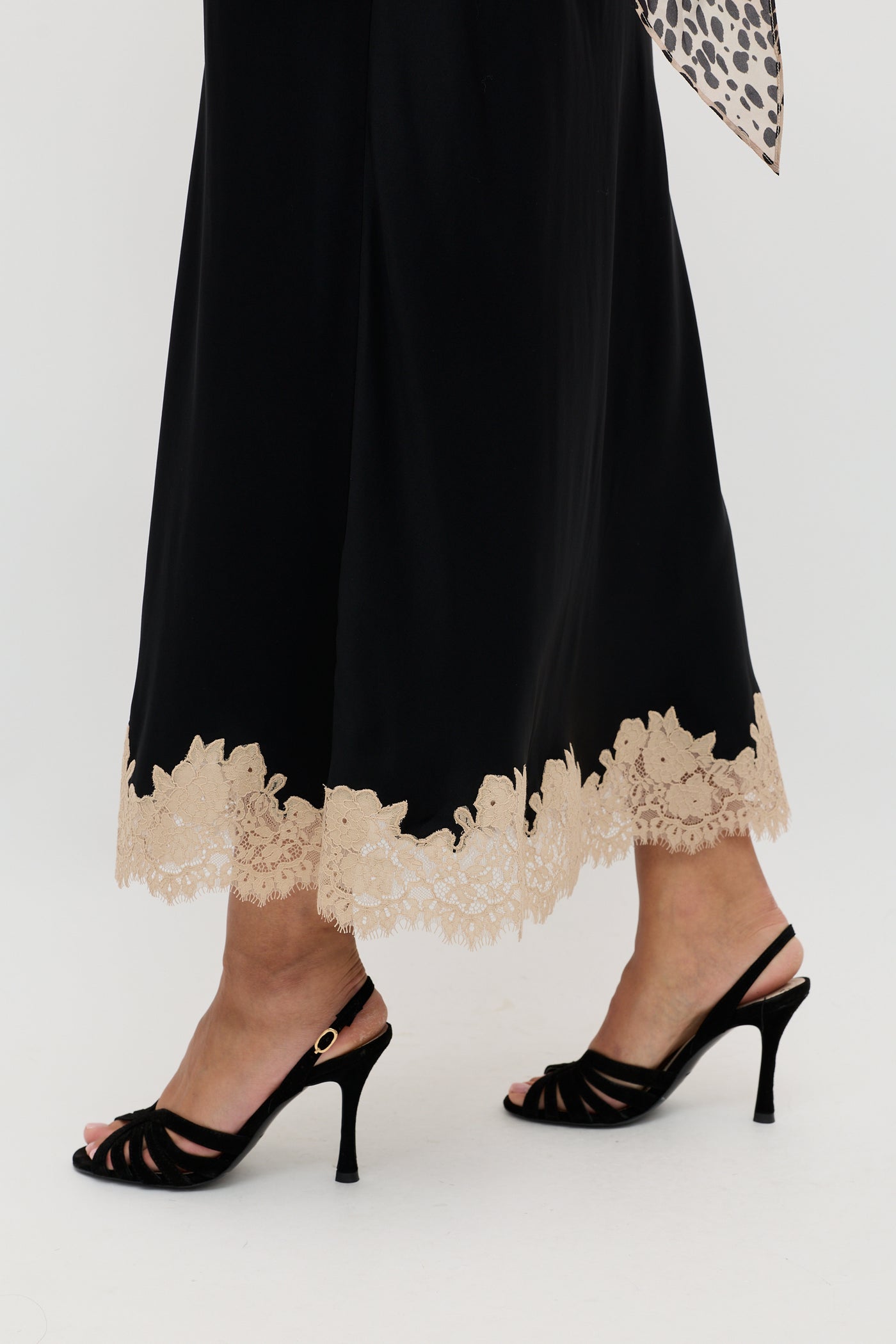 A person wearing the Matilde - Black long skirt with beige lace trim at the hem and black high-heeled sandals, standing on a white background.