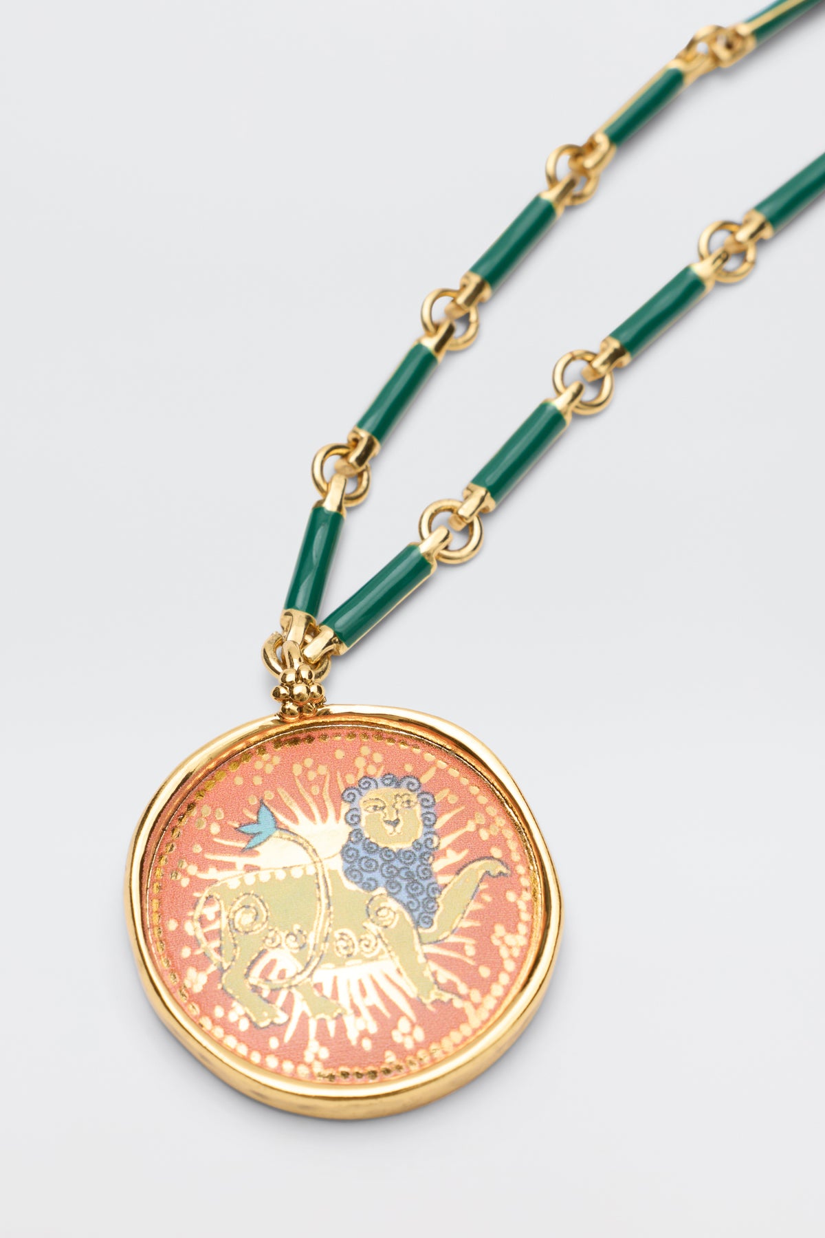 Elevate your style with the Ari - Astro Leo necklace, featuring a bold gold and green chain and a statement disc charm. The round pendant displays a striking blue and gold lion on a coral background, framed in polished gold—making it the perfect zodiac necklace to stand out.
