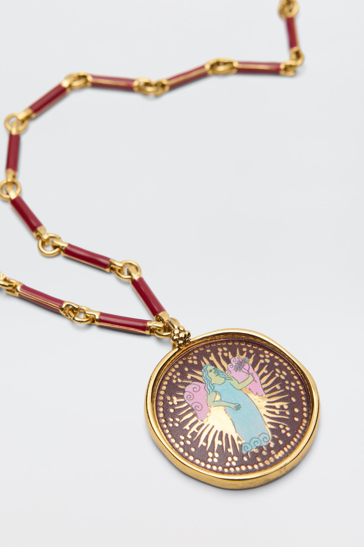 Introducing the Ari - Astro Virgo: a gold pendant necklace with bold red links, featuring a striking statement disc charm adorned with an artistic image of a blue and green Virgo figure surrounded by radiant gold rays against a dark background—an eye-catching piece that makes for the perfect zodiac necklace.