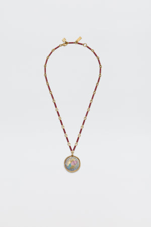 The Ari - Astro Aquarius necklace features gold zodiac detailing, red cylindrical beads, small gold spacers, and a statement disc charm with a colorful, intricate design at the center. Displayed against a plain white background.