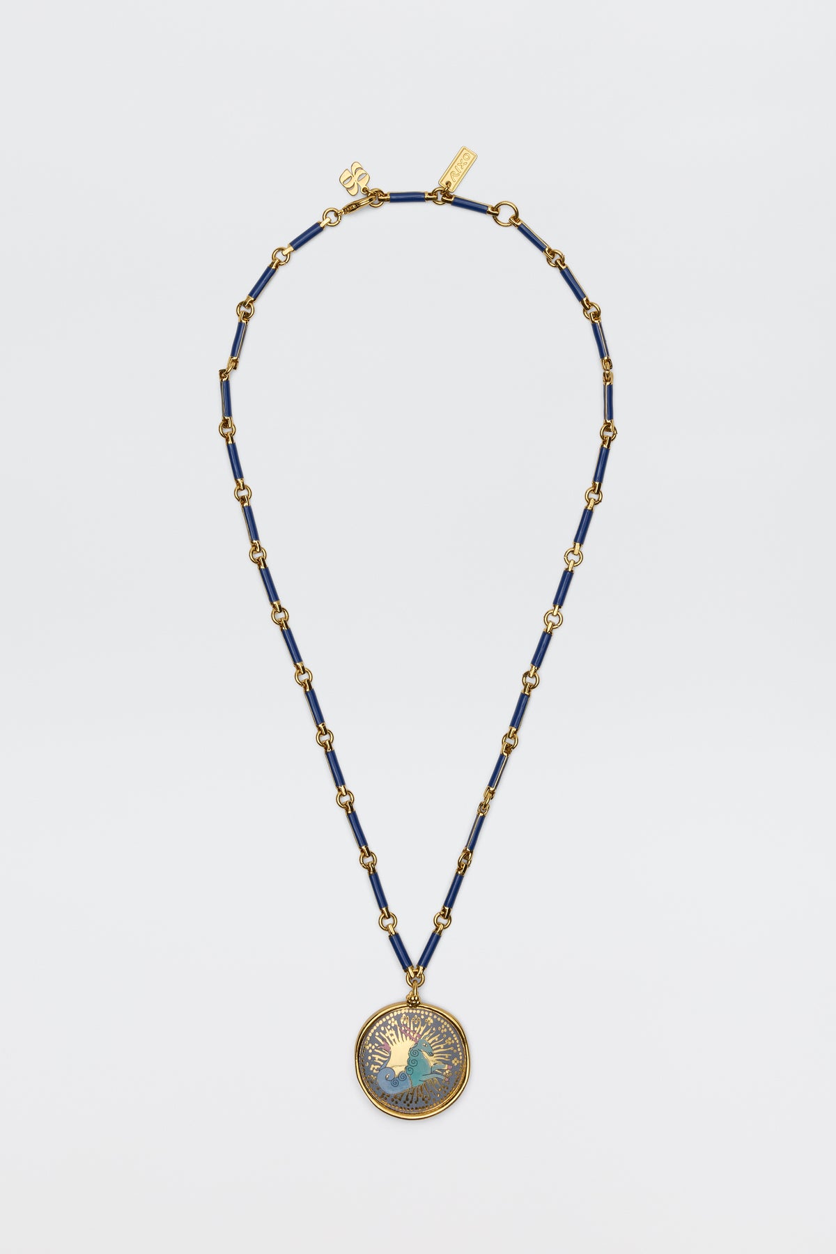 The Ari - Astro Capricorn necklace features gold and navy blue beads with a statement disc charm of a woman’s profile and radiating rays, shown against a plain white background.