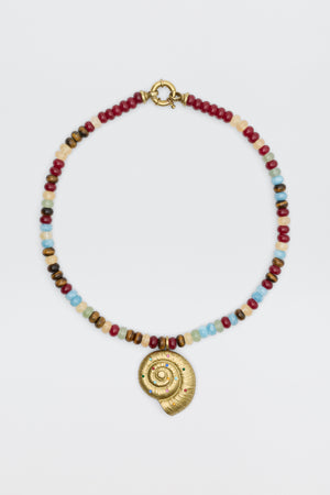 The Parma - Multi beaded necklace showcases red, blue, brown, and white beads with a gold spiral shell pendant adorned with small colored gemstones, elegantly displayed on a white background.
