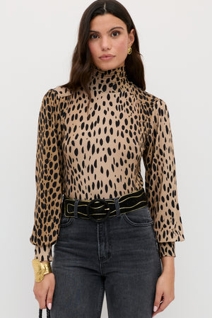 A woman with long dark hair wears the Suki - Antelope Spot Black top, black jeans, a black belt with a gold buckle, and gold accessories, standing against a plain white background.