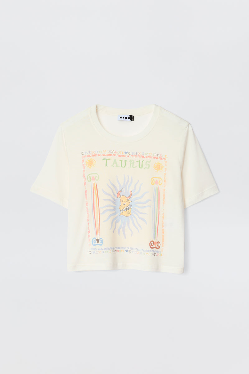 The Ria - Taurus is a cream short-sleeve tee with a vibrant Taurus illustration, astrological symbols, sun rays, and pastel decorative borders—ideal for pairing with RIXO skirts.