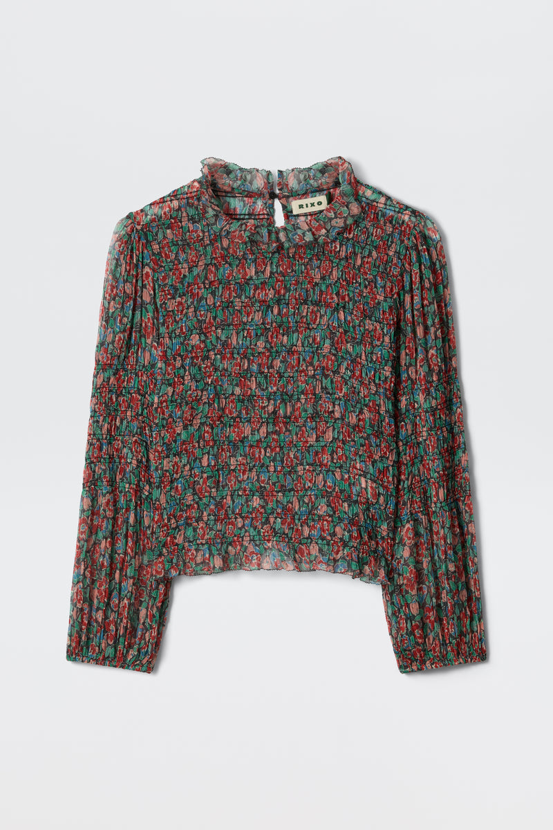 The Gardenia - Jeannie Bloom Charcoal is a sheer, long-sleeve blouse with a high ruffled collar and red and green floral pattern on black, shown flat on a white surface.