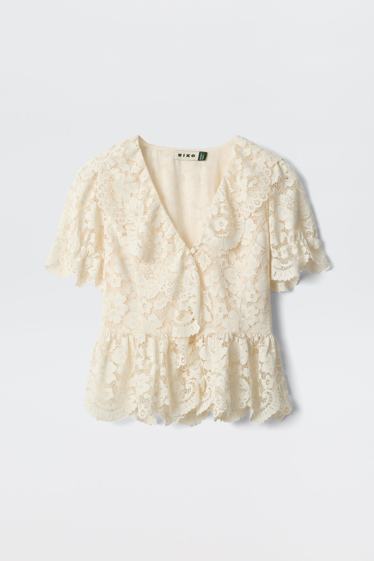 Dollie - Cream: A cream-colored lace blouse featuring short sleeves, a V-neckline, ruffled hem, and scalloped edges, shown against a plain white background.