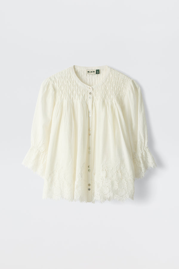 The erika top ivory is a white, long-sleeved blouse featuring a round neckline, button-down front, and delicate lace embroidery on the sleeves and hem. Its lightweight fabric has a subtly textured yoke.