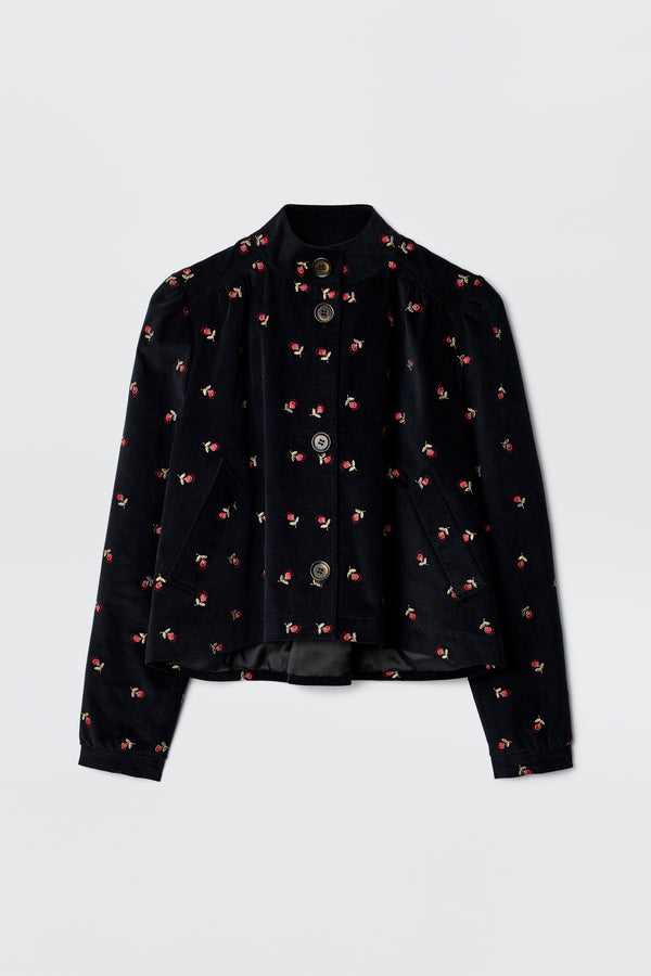 The Nyla - Dandy Embroidery Deep Navy is a 60s-inspired black velvet jacket with long sleeves, a mandarin collar, silver front buttons, and scattered pink and red floral embroidery.