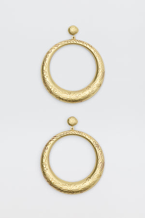The Sian - Gold earrings are large, circular gold hoops with intricate engraved floral and swirl patterns. Each earring features a round stud top connected to a wide open hoop, displayed on a plain white background.