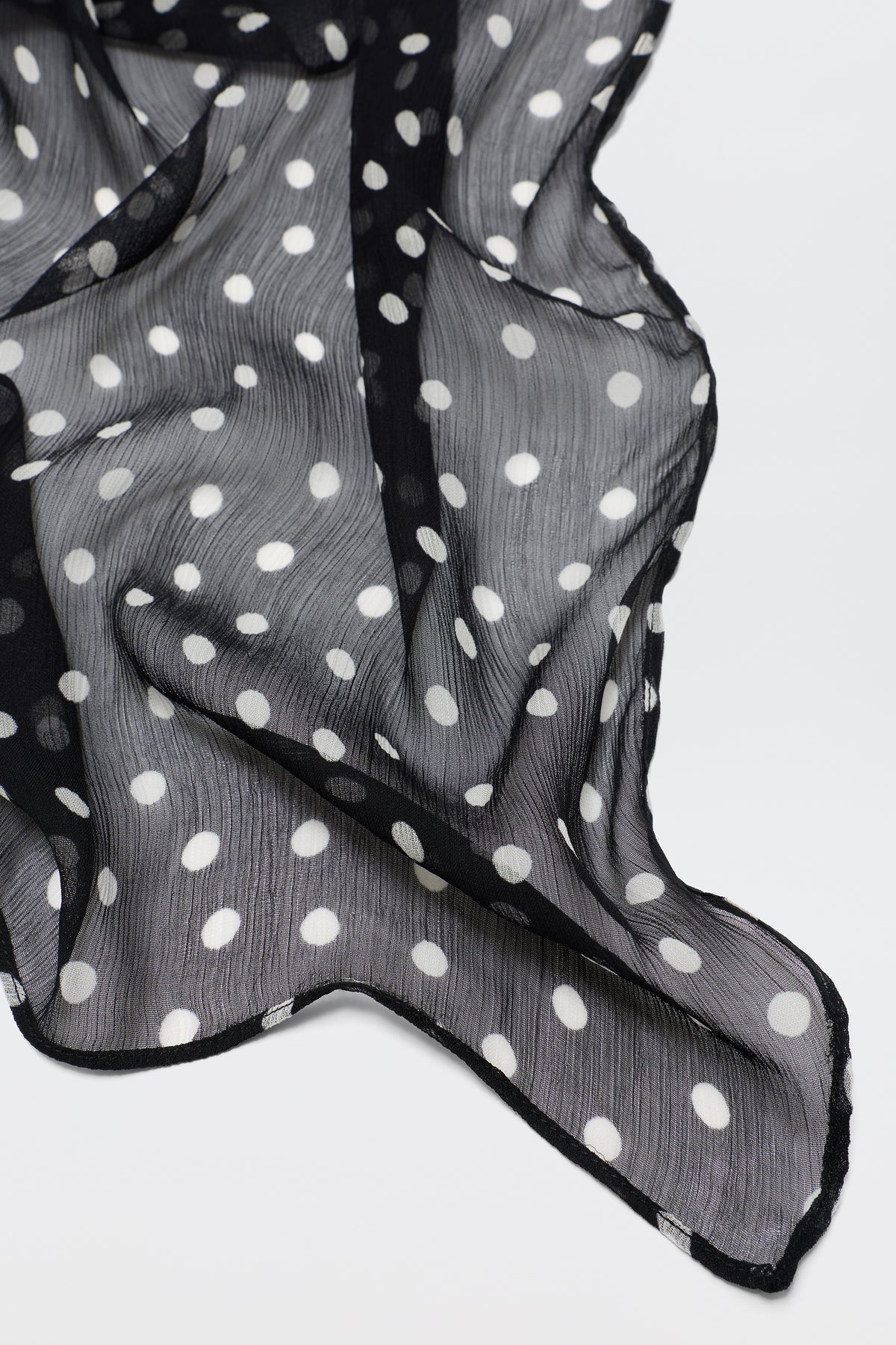 A sheer deep navy Julien - Emma Spot scarf with white polka dots is draped in gentle folds on a light background, showing its slightly textured look and flowing, lightweight feel.