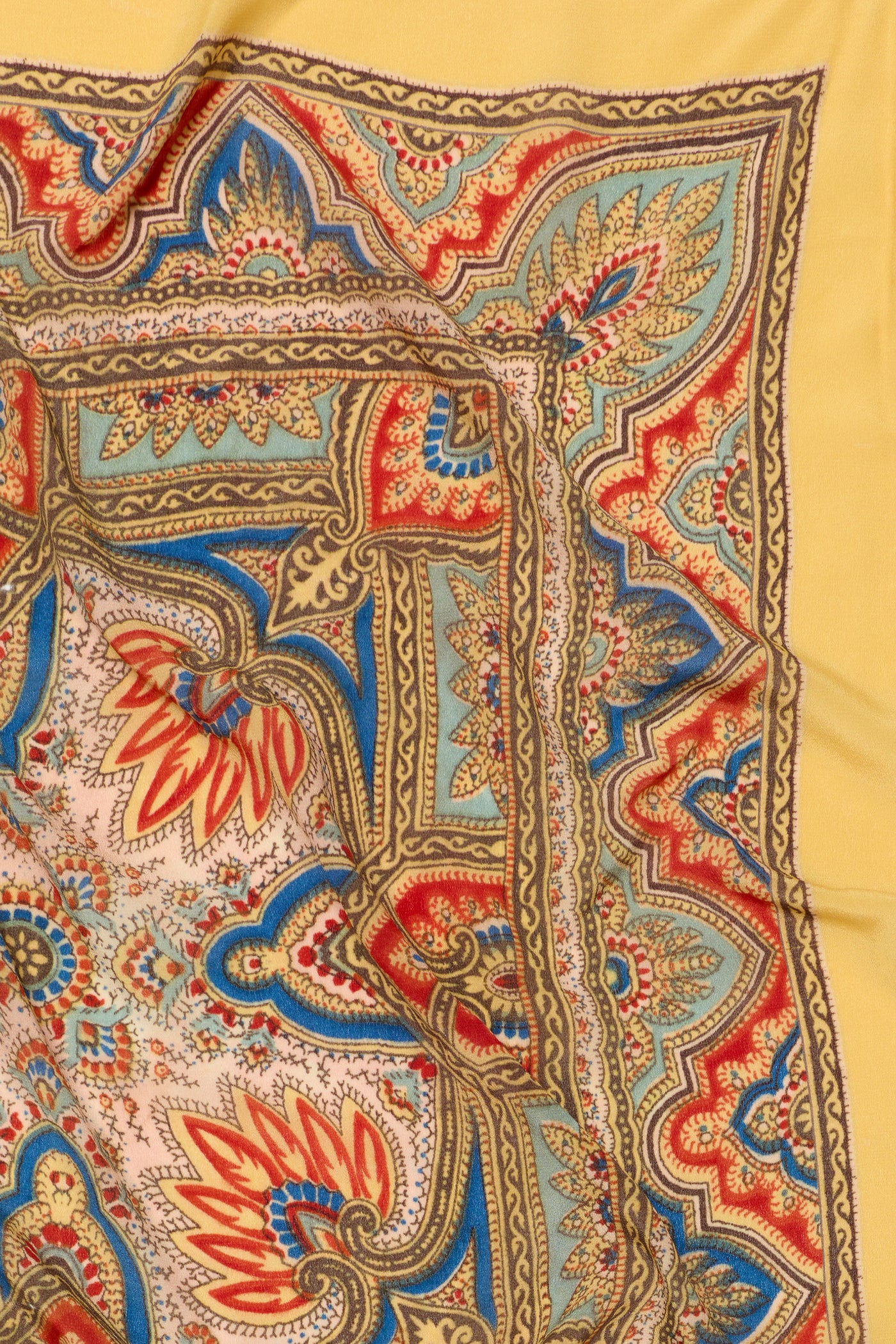 The Menno - Paisley Golden silk scarf showcases a colorful paisley pattern with intricate red, blue, yellow, and green designs set against a golden yellow background; its detailed motifs and folded corner make it a vibrant fashion accessory perfect for adding flair to any ensemble.