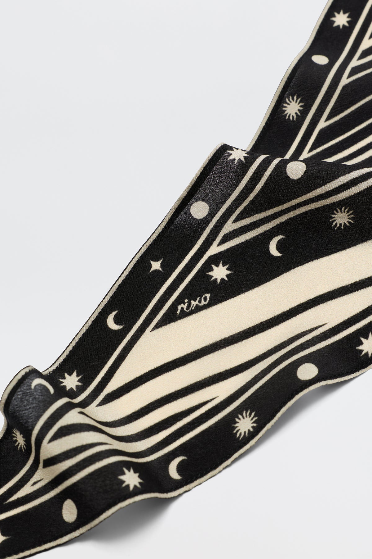 A close-up of the chic Nara - Starstruck Black scarf shows its celestial star, moon, and line pattern in black and white, with "RIXO" within the design. The pure silk fabric looks soft and subtly wavy.