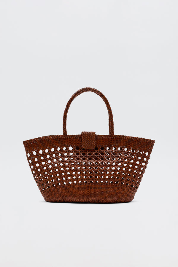 The Lucine - Tan is a brown woven straw tote bag with an openwork pattern, two handles, and a small flap closure, shown against a plain white background.