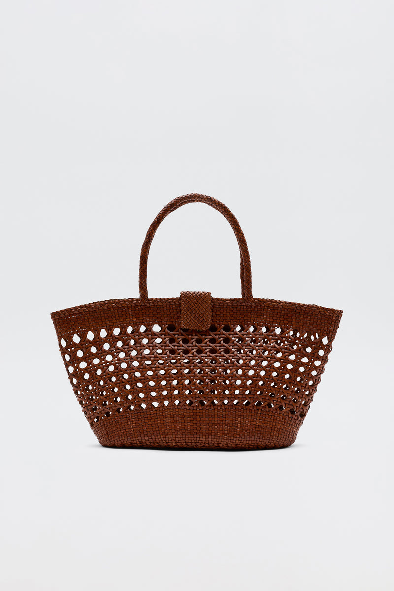 The Lucine - Tan is a brown woven straw tote bag with an openwork pattern, two handles, and a small flap closure, shown against a plain white background.