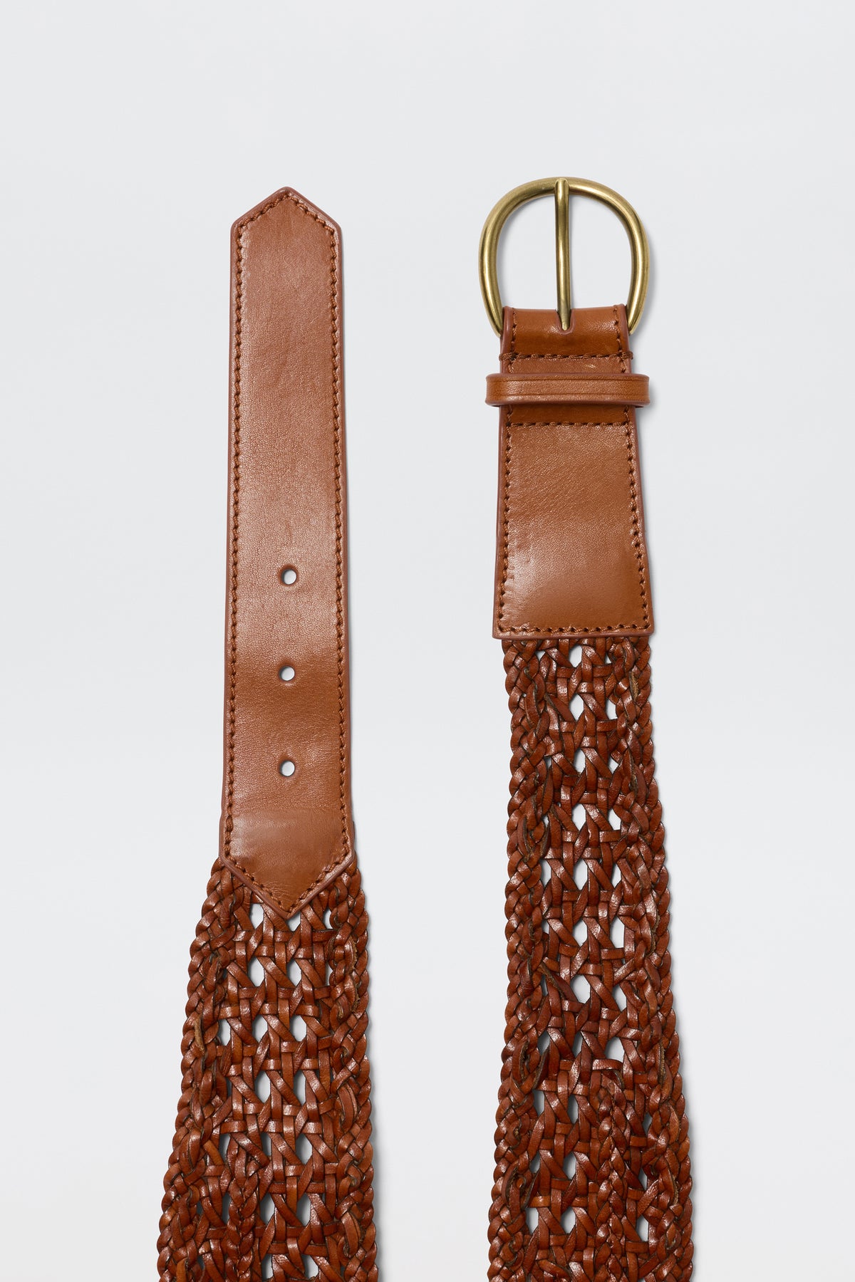 A close-up of the Roxella - Tan belt, featuring brown woven leather with a gold buckle and smooth ends with fastening holes. This classic accessory is displayed against a plain white background.