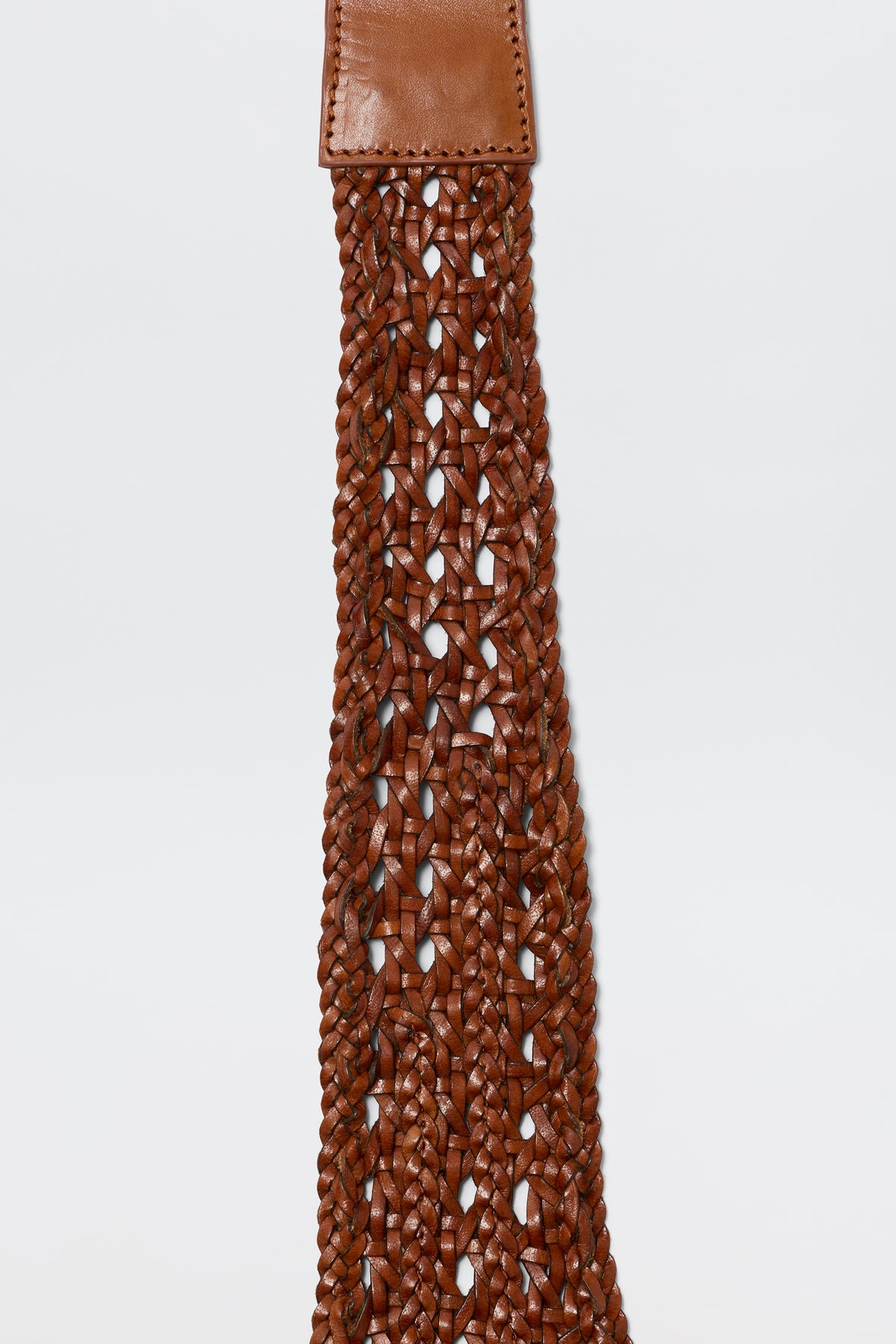 Close-up of the Roxella - Tan belt, featuring a brown woven braided pattern and stitched leather end, perfect as a stylish waist accessory, shown against a plain white background.