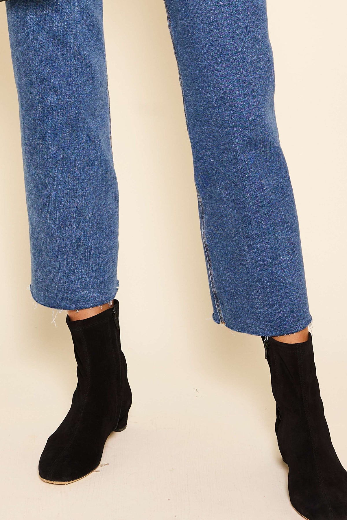 A person stands on a light floor wearing blue jeans with frayed hems and vintage-inspired Rey - Black boots with a feminine heel; only their legs and feet are visible.