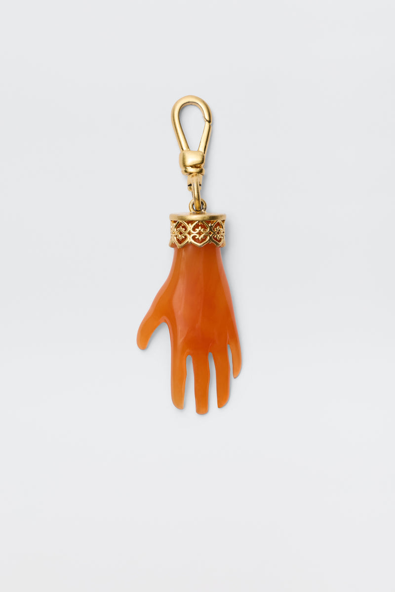 The Hand - Orange keychain features an orange, gold-plated hand charm with a gold ornate band at the wrist, attached to a gold lobster clasp. Shown against a plain white background.
