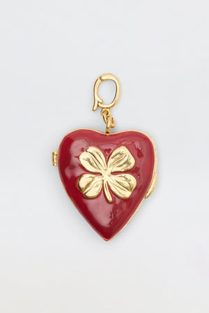 The Ardina - Red is a heart-shaped red locket featuring a gold four-leaf clover on the front and a gold clasp, displayed on a plain white background.