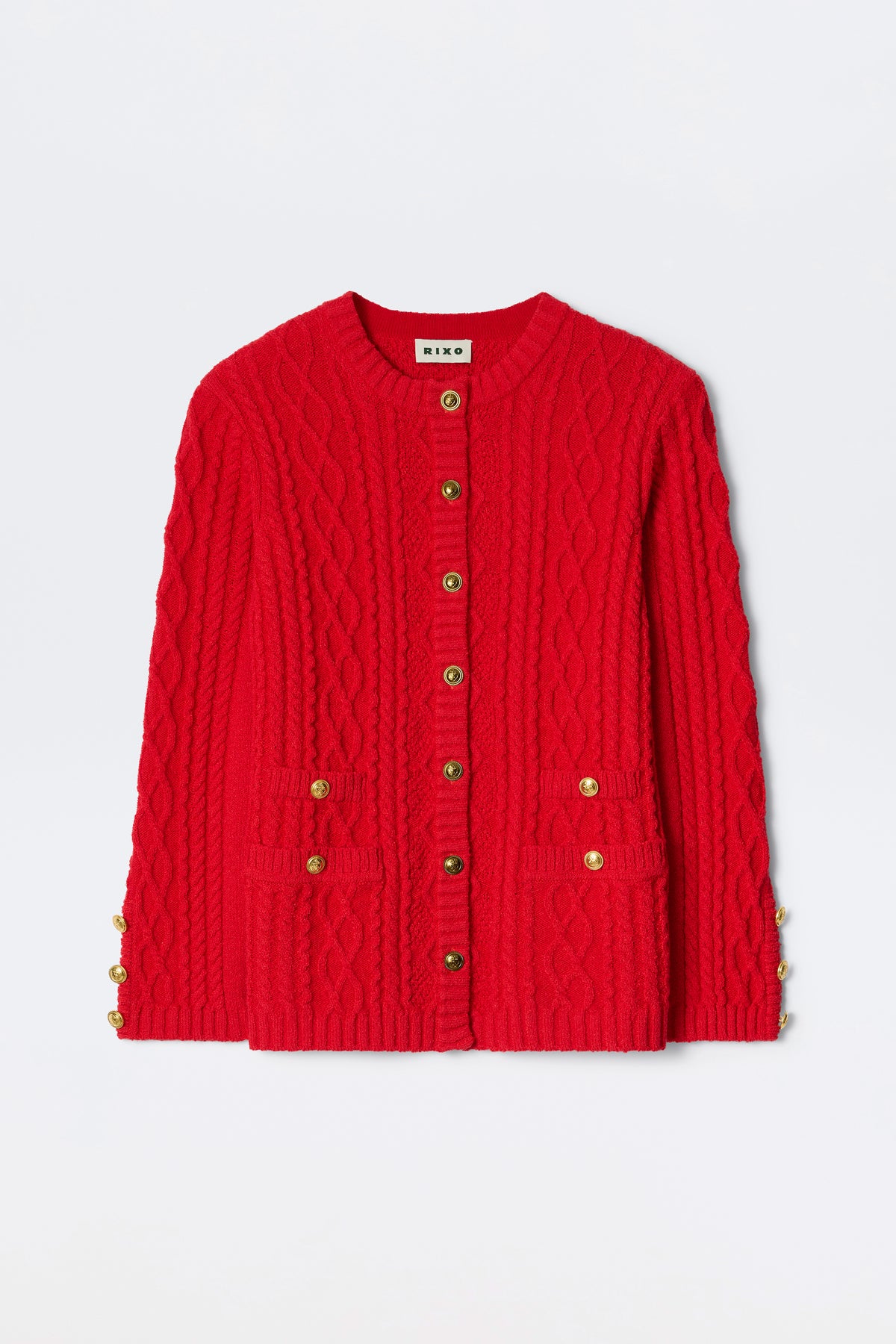 The Maurya - Red is a bright red cable-knit cardigan with gold buttons on the front and sleeves, plus two front pockets, shown against a plain white background.
