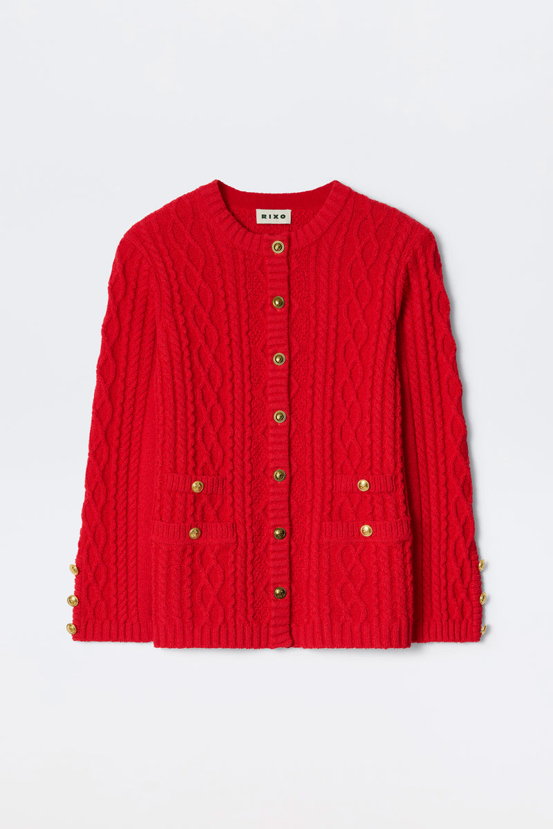 The Maurya - Red is a bright red cable-knit cardigan with gold buttons on the front and sleeves, plus two front pockets, shown against a plain white background.