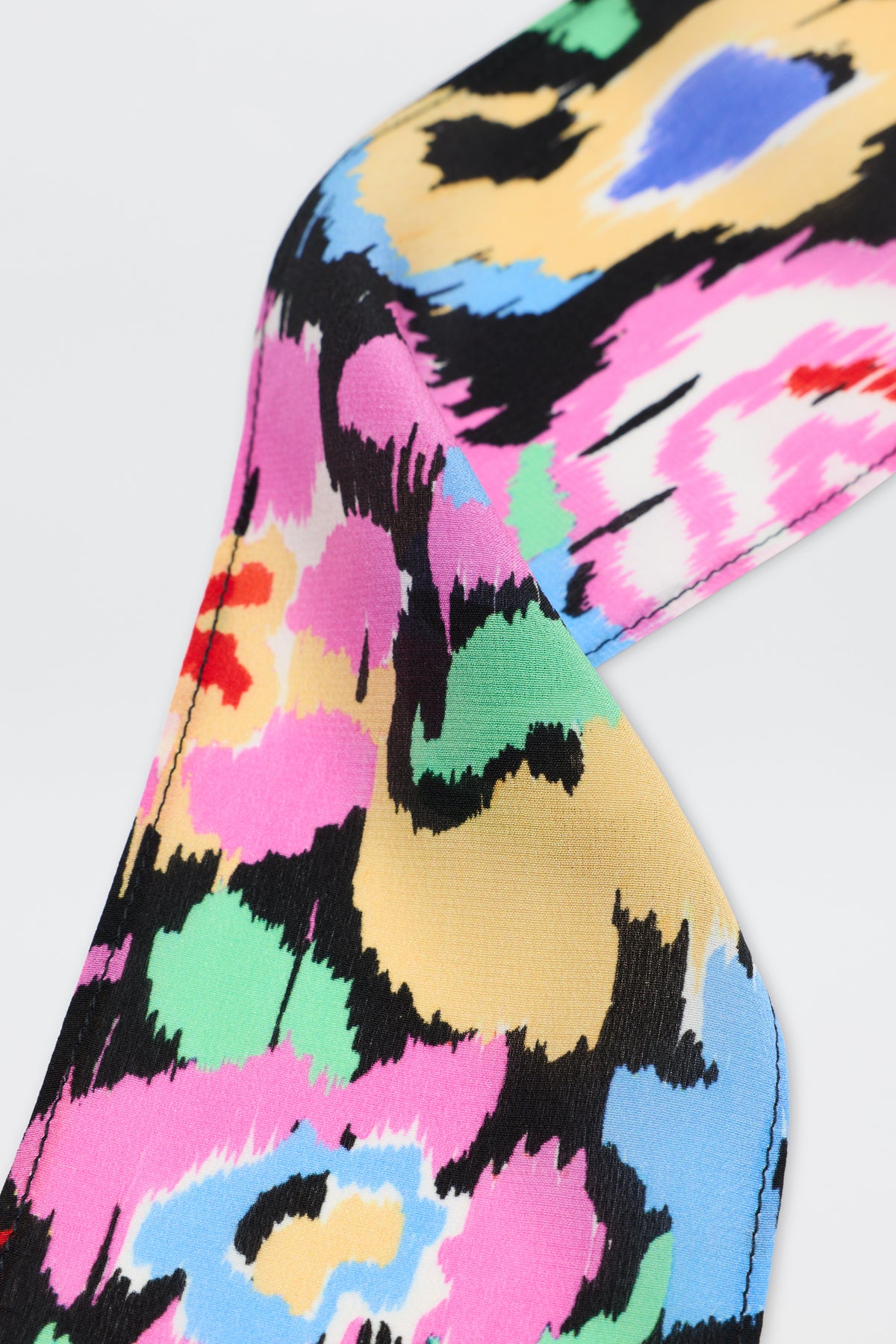 A close-up of Alexa - Ikat Bloom Charcoal fabric, showcasing a colorful abstract pattern with splashes of black, yellow, pink, green, blue, and white on a smooth surface.