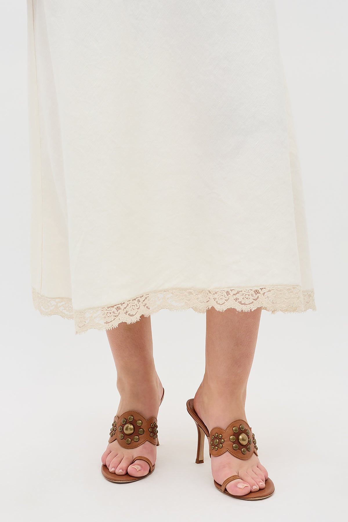 A person wearing a long white skirt with lace trim and Esmeray - Tan heeled sandals, standing against a plain white background.