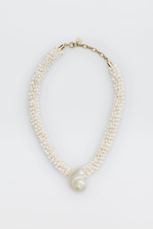 Imara - Pearl: A beaded necklace with small white beads, a large spiral seashell pendant, gold clasp, and adjustable chain, displayed on a white background.