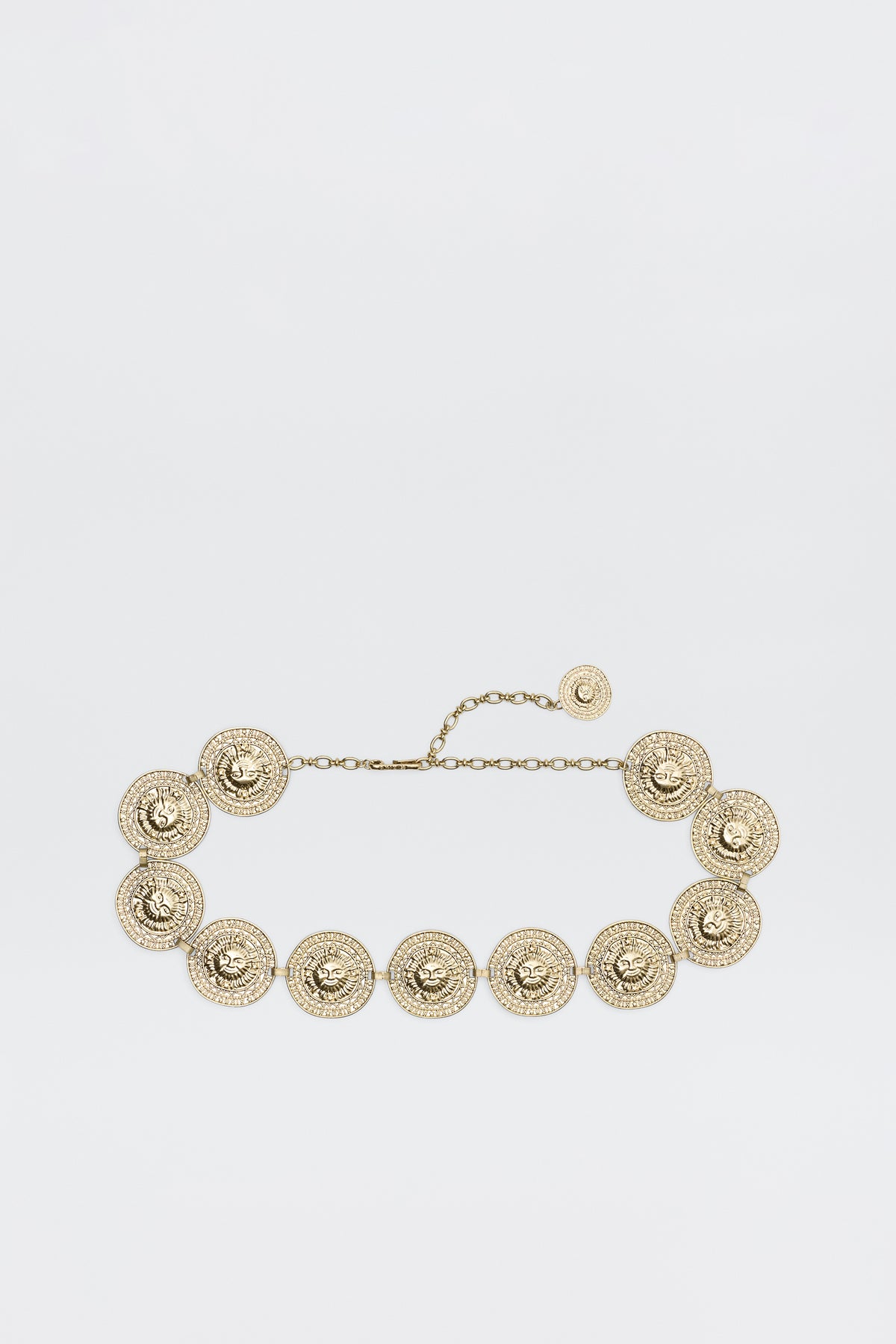 Leyla - Gold is a gold chain belt with round, ornate medallions linked together, each featuring intricate textured detailing and an adjustable chain clasp, shown on a plain white background.