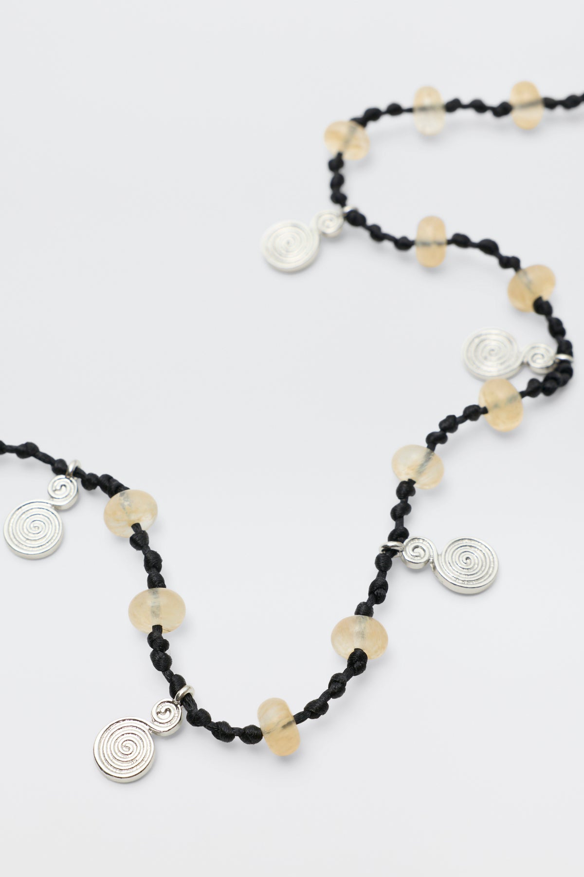 Mikah - Silver: A black knotted necklace featuring round translucent yellow beads and spiral silver charms spaced along its length, displayed on a white background.