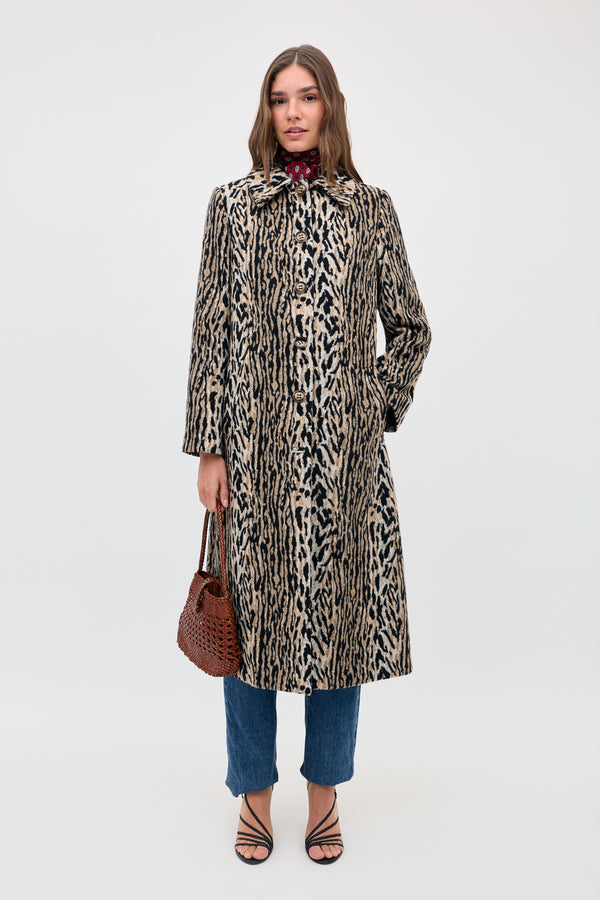 A woman in the Milly - Bohemia Leopard coat over blue jeans and black strappy sandals holds a brown woven handbag, facing the camera against a plain white background.